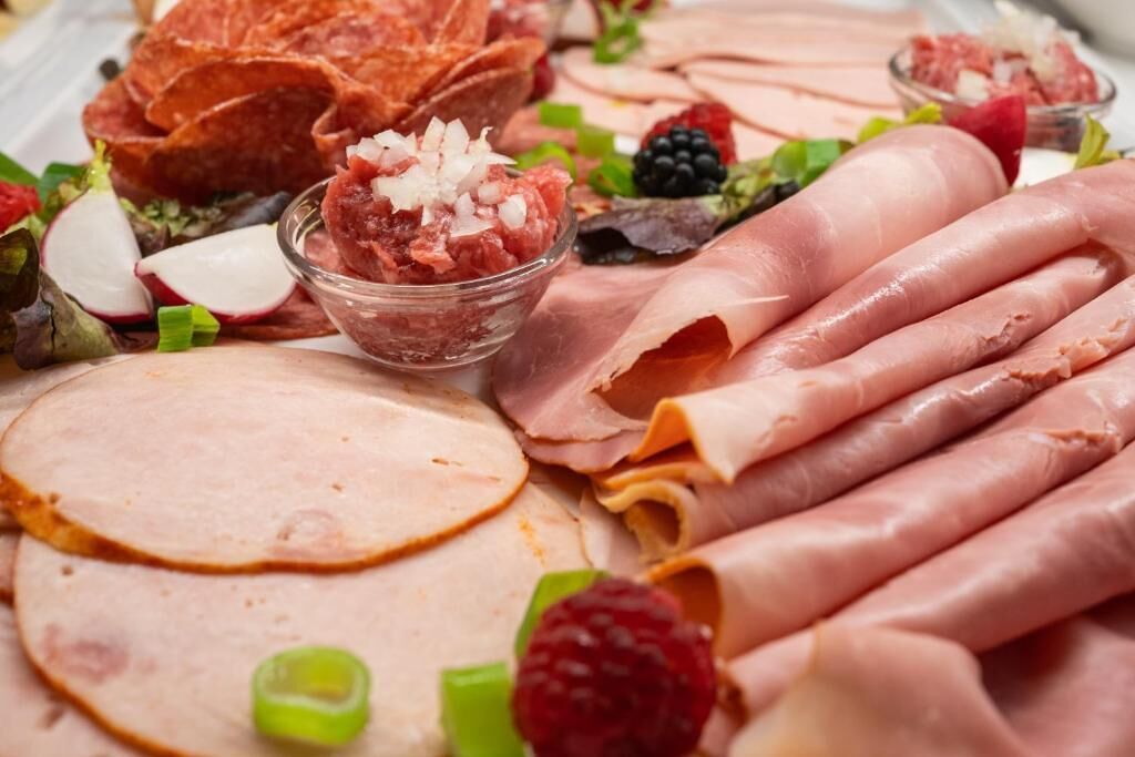 A variety of meats including sliced ham, prosciutto, and other deli items, accompanied by fresh fruits and vegetables.