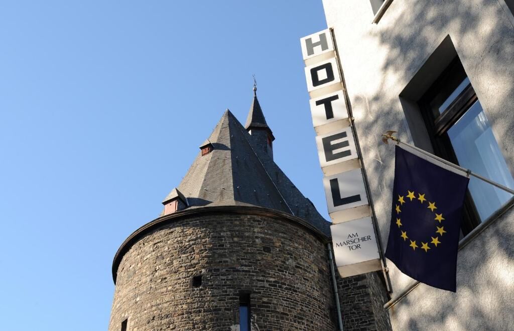 Un letrero de hotel con la palabra 'HOTEL' y 'AM MARSCHIER TOR' escritas, y la bandera de la Unión Europea.