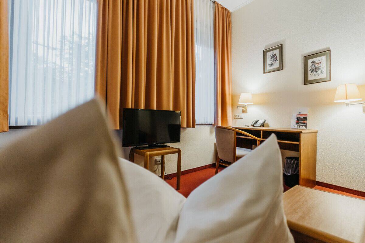 Una habitación de hotel con cama, televisión, escritorio con silla y lámpara.