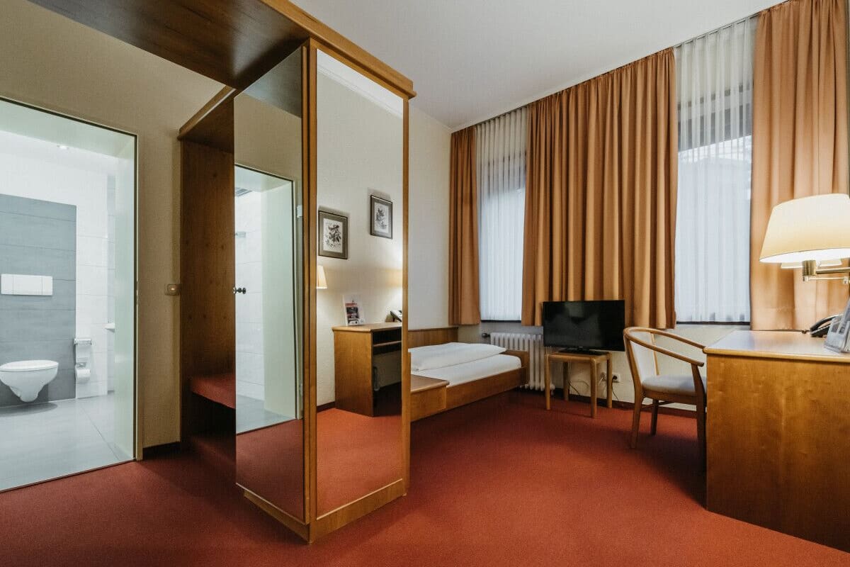 Una habitación de hotel con cama, escritorio, silla, televisor y espejo.