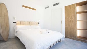 Un dormitorio con cama, cabecera de madera, una tabla de surf, armario y vestidor con puertas correderas.