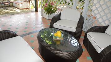 Un patio con mobiliario de mimbre, una mesa de vidrio con limones y una valla de celosía blanca.