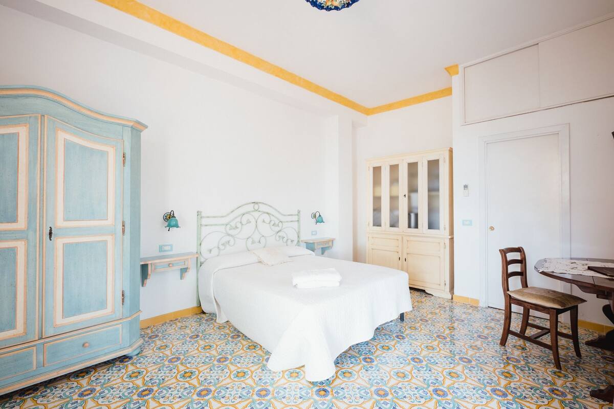 Un dormitorio con cama, armario, una mesita y una silla.