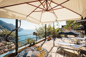 A terrace with a view of the sea, outdoor furniture, and potted plants.