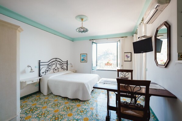 A bedroom with a bed, a desk, a chair, a TV, and a window with a view.