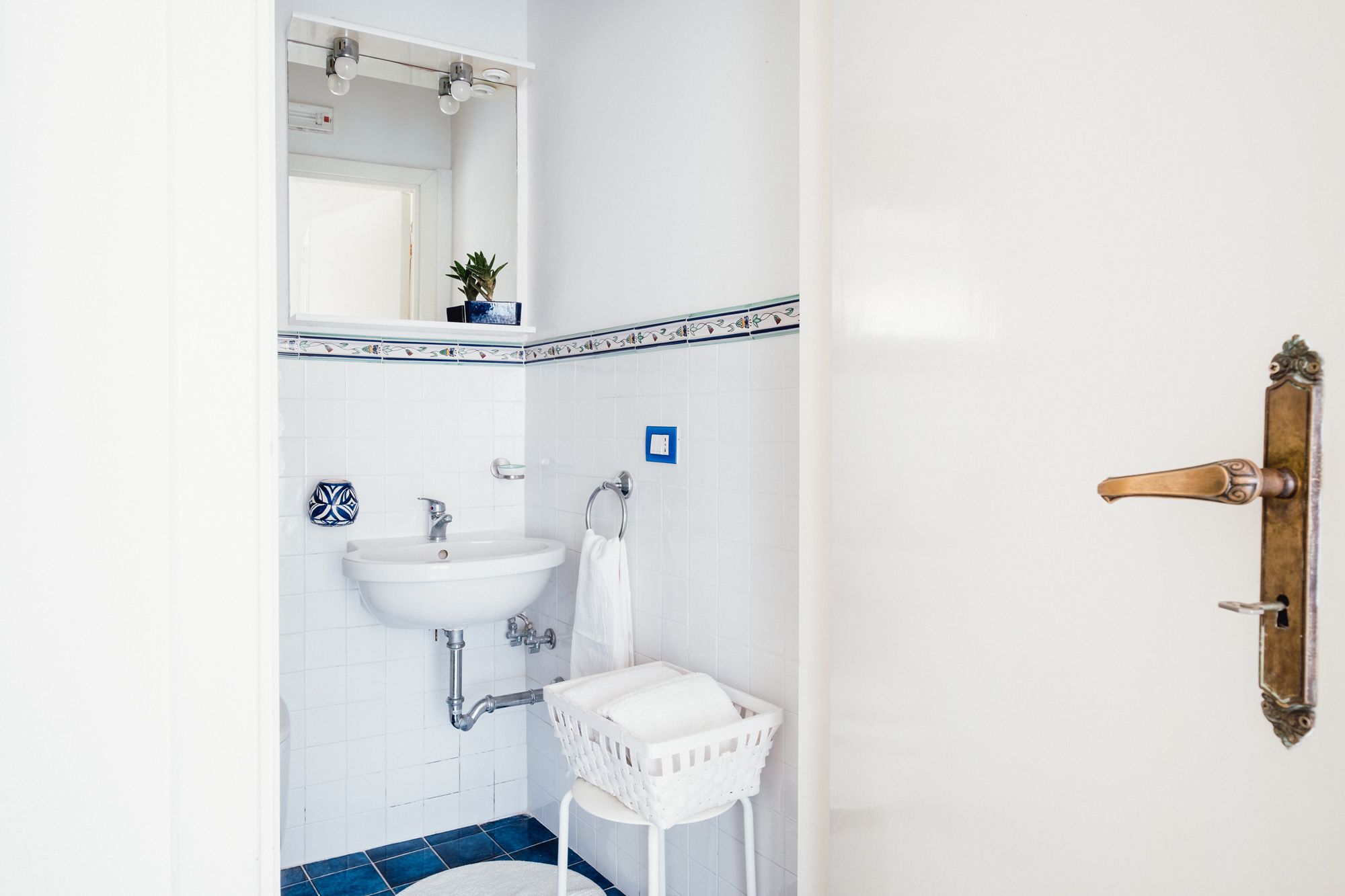 Un baño con lavamanos blanco, un espejo, un perchero y una cesta blanca.