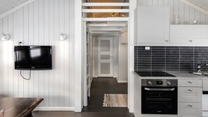 Une cuisine moderne avec des meubles blancs, un four encastré et un téléviseur à écran plat fixé au mur.