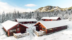 Un chalet enneigé comprenant plusieurs cabanes, un réfectoire central et un paysage de montagne en toile de fond.