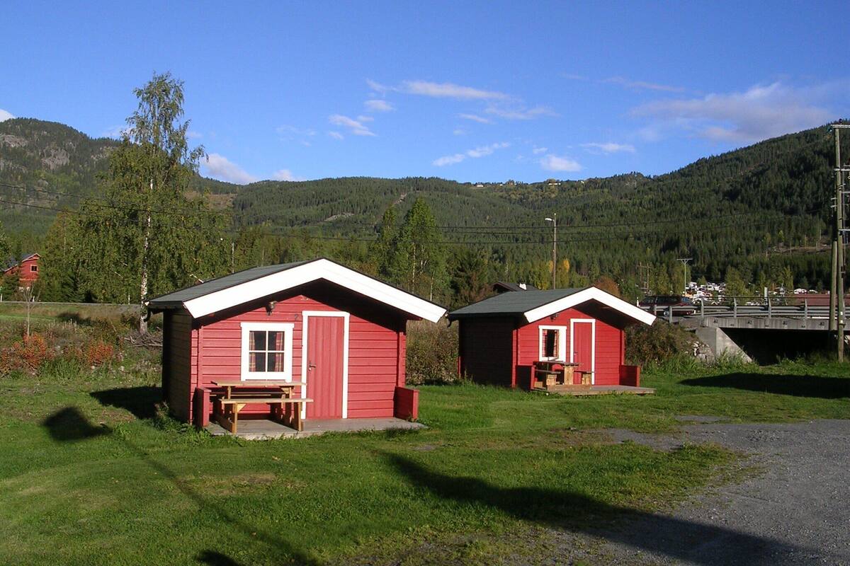 Two red cabins with white trim, a picnic table, and a grassy area in a mountainous setting.