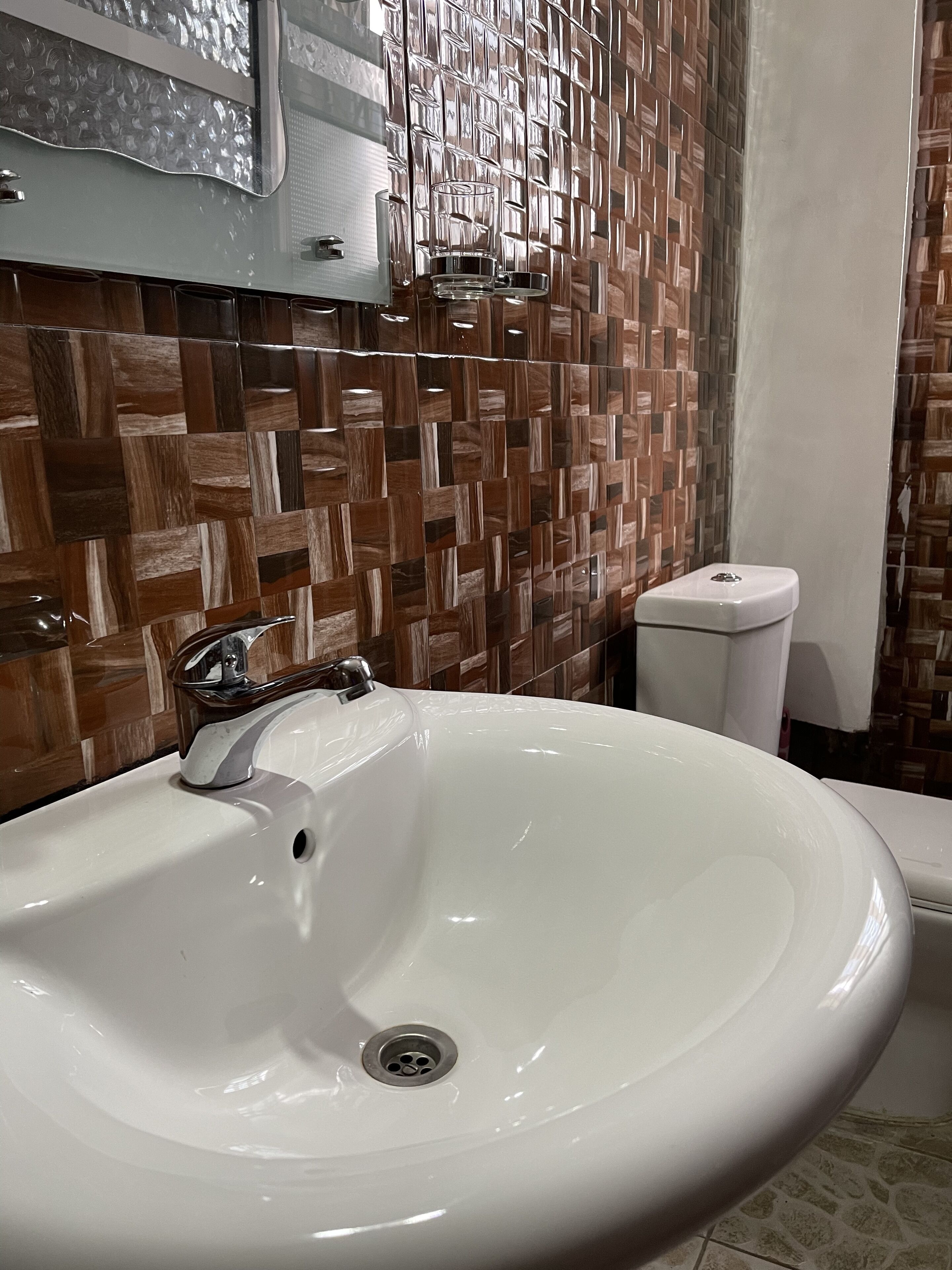 A bathroom with a white sink, a mirror, and a toilet. The wall has a wooden pattern design.