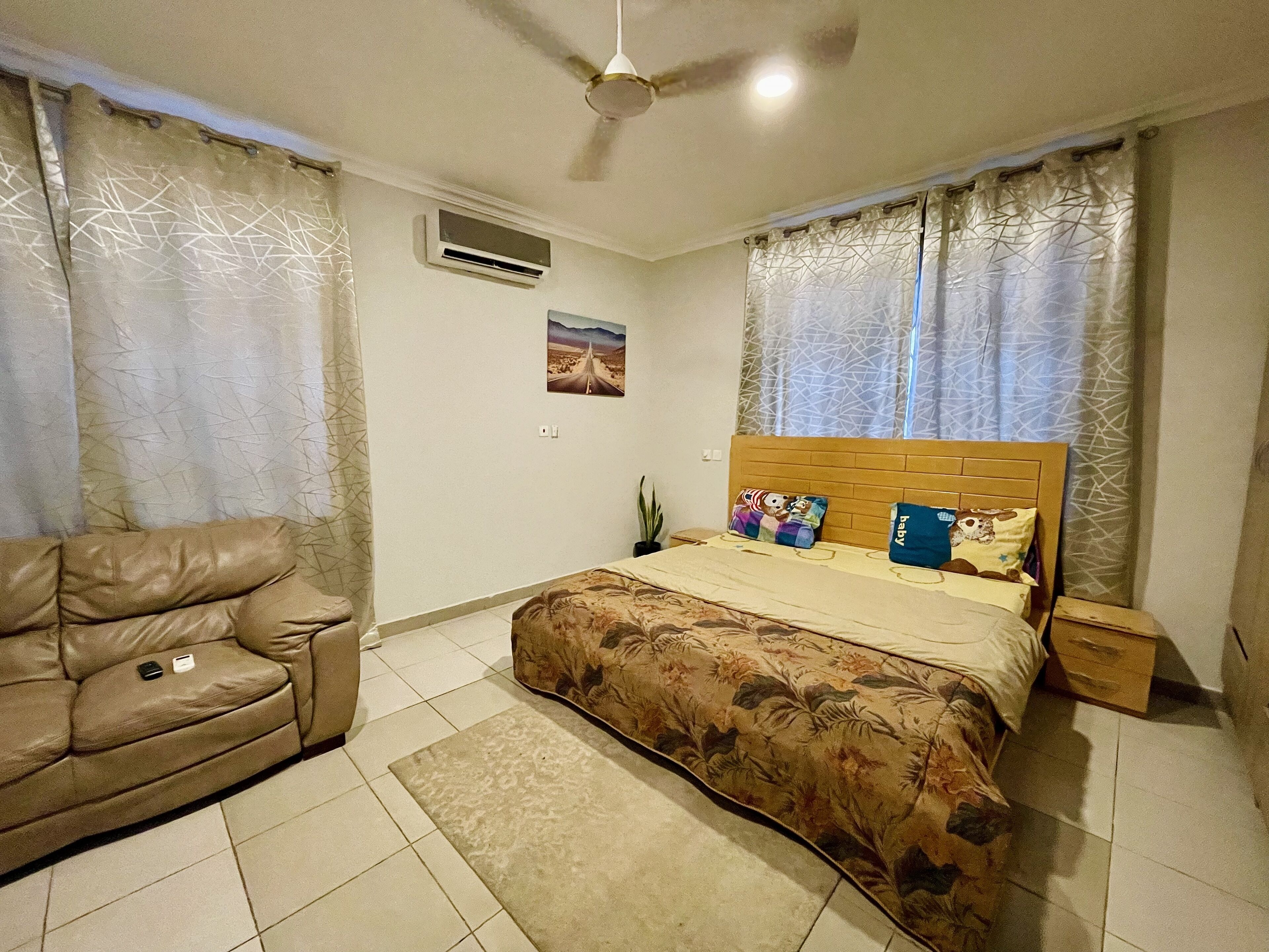 A bedroom with a bed, a sofa, a ceiling fan, and an air conditioning unit.