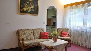 En stue med sofa, stol, et lille bord med en vase og et maleri på væggen.