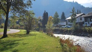 En græsplæne med en flod, træer og huse i baggrunden.