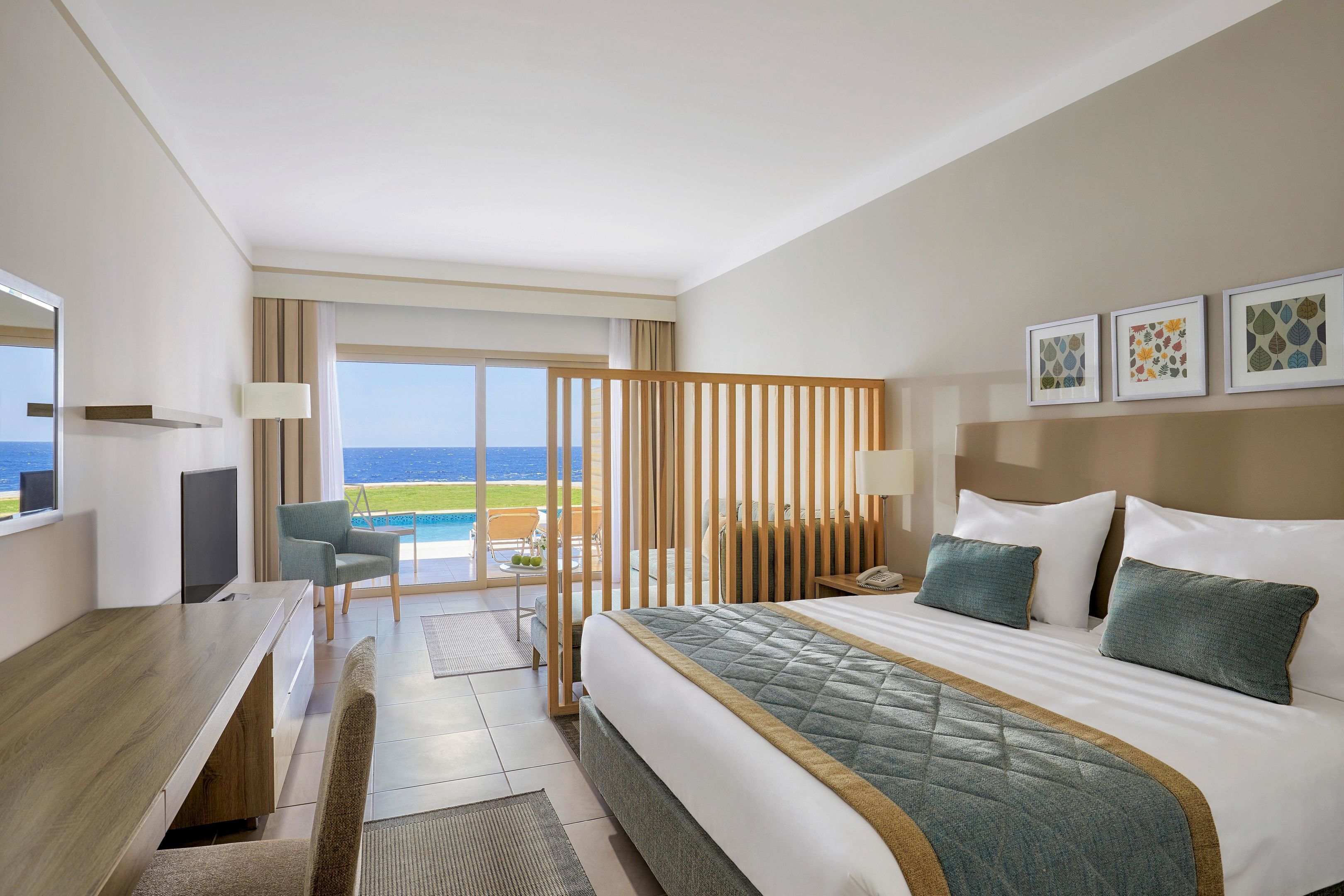 A hotel room with a bed, a desk, a chair, a TV, and a view of the ocean.