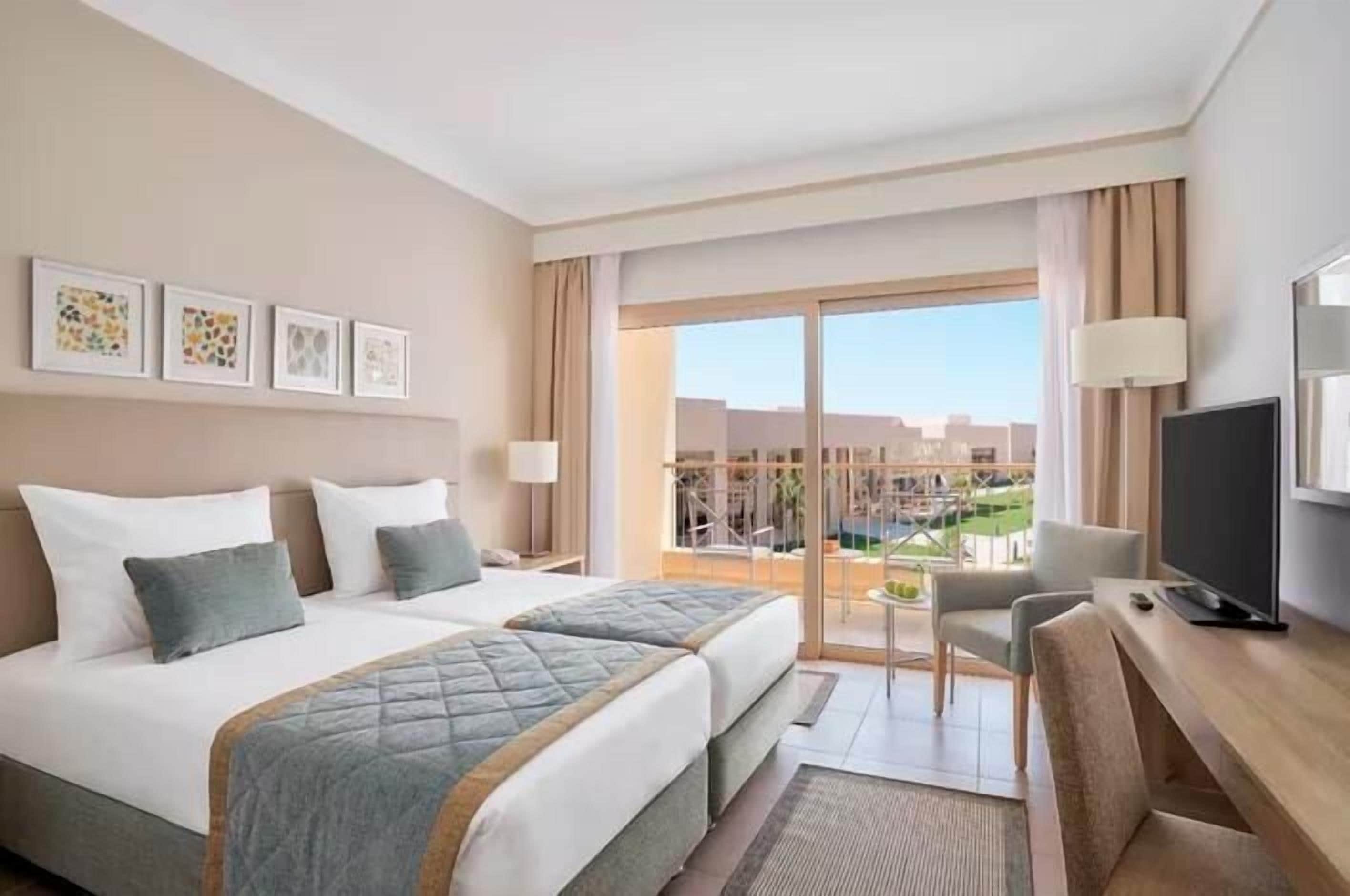 A hotel room with a bed, a desk, a chair, a TV, and a balcony with a view.