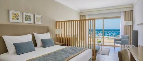 A hotel room with a bed, a desk, a chair, a TV, and a balcony with a view of the sea.
