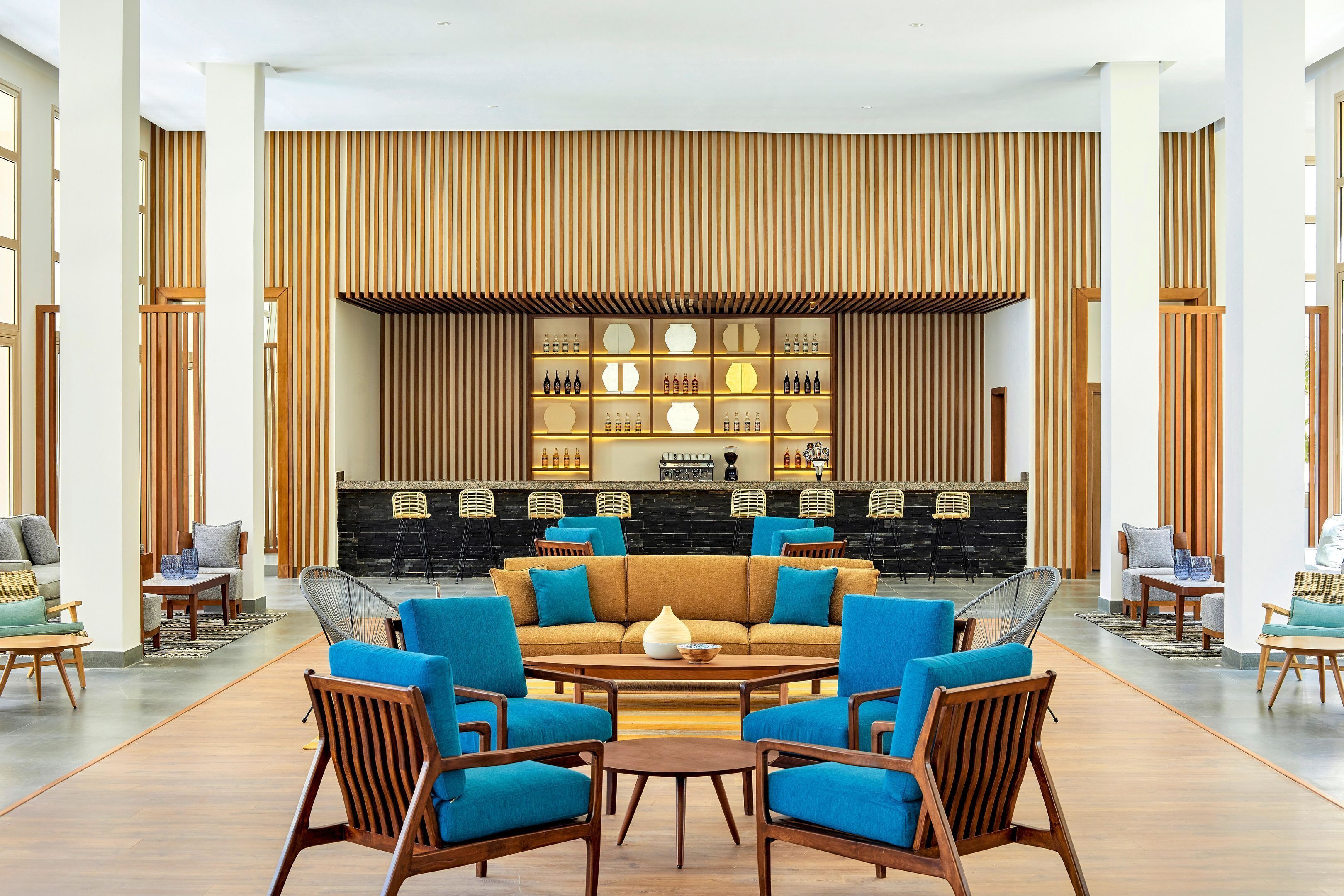 Un hall d'entrée moderne avec un espace salon central, un bar doté d'étagères remplies de bouteilles et un mur en lambris de bois.