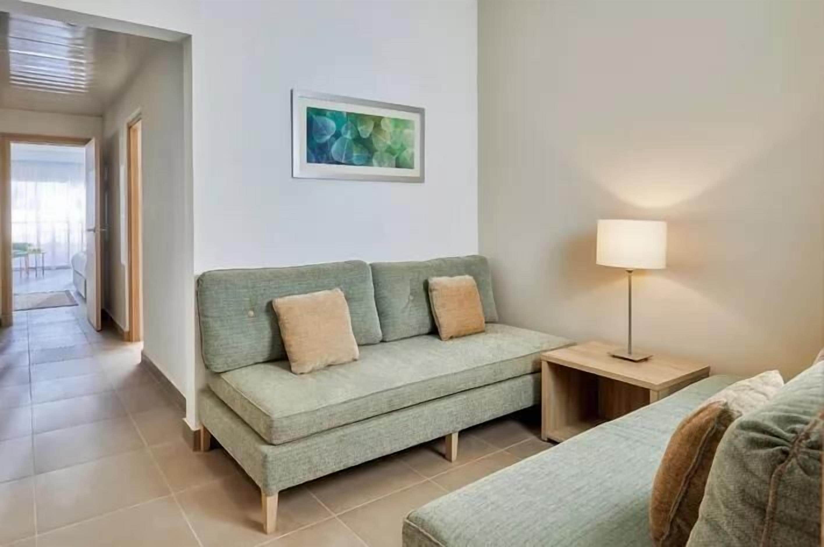 A living room with a sofa, a side table with a lamp, and a framed picture on the wall.