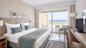 Een hotelkamer met een bed, een bureau, een televisie en een balkon met uitzicht op de oceaan.