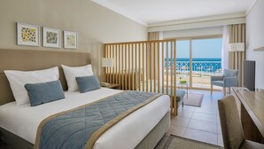 Een hotelkamer met een bed, een bureau, een stoel en uitzicht op zee.