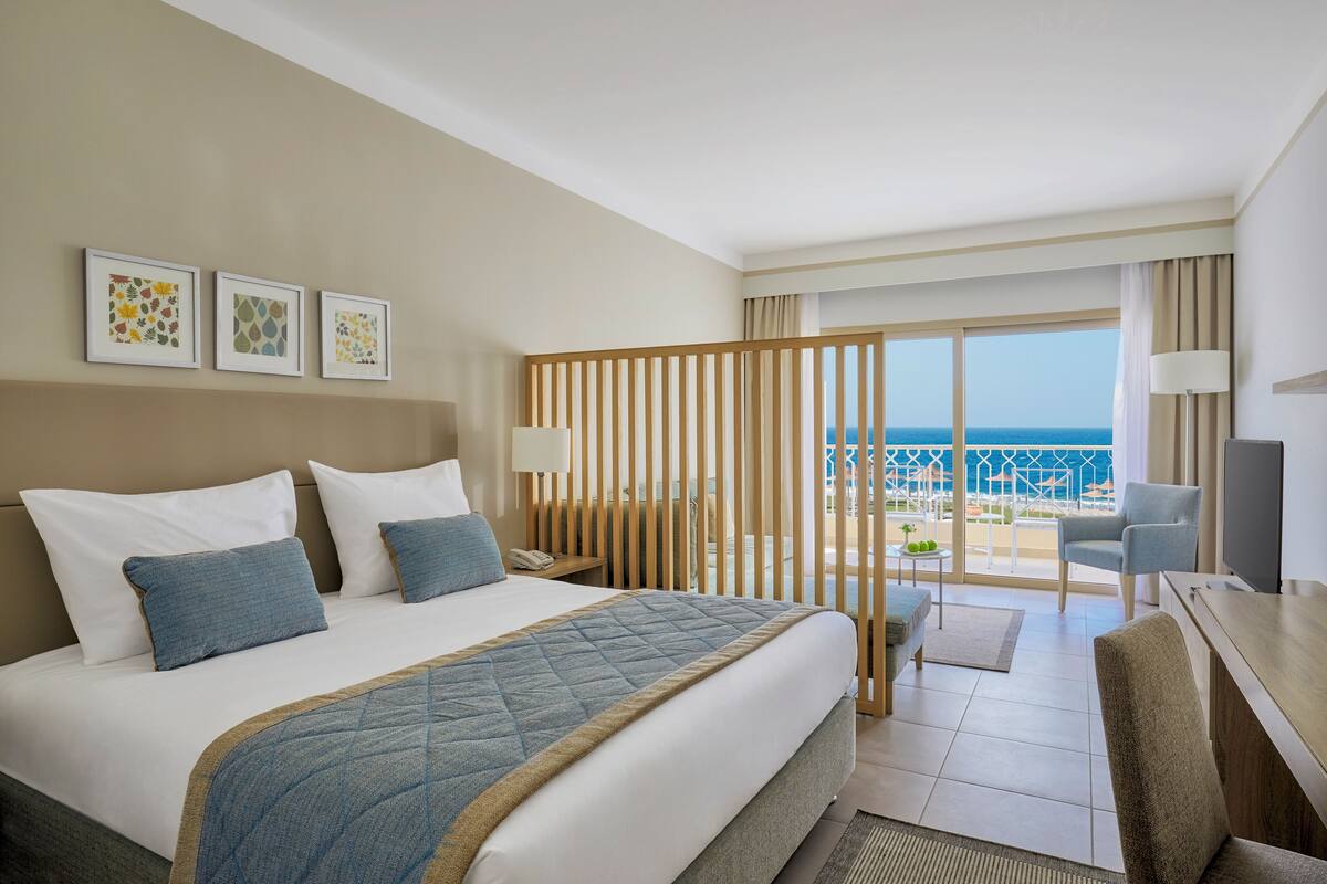 A hotel room with a bed, a desk, a chair, and a view of the ocean.