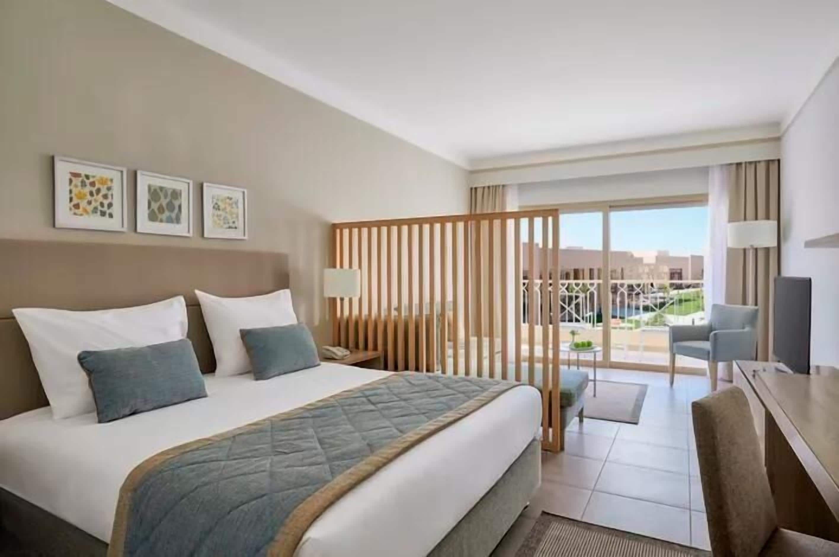 A hotel room with a bed, a desk, a chair, a TV, and a balcony with a view.