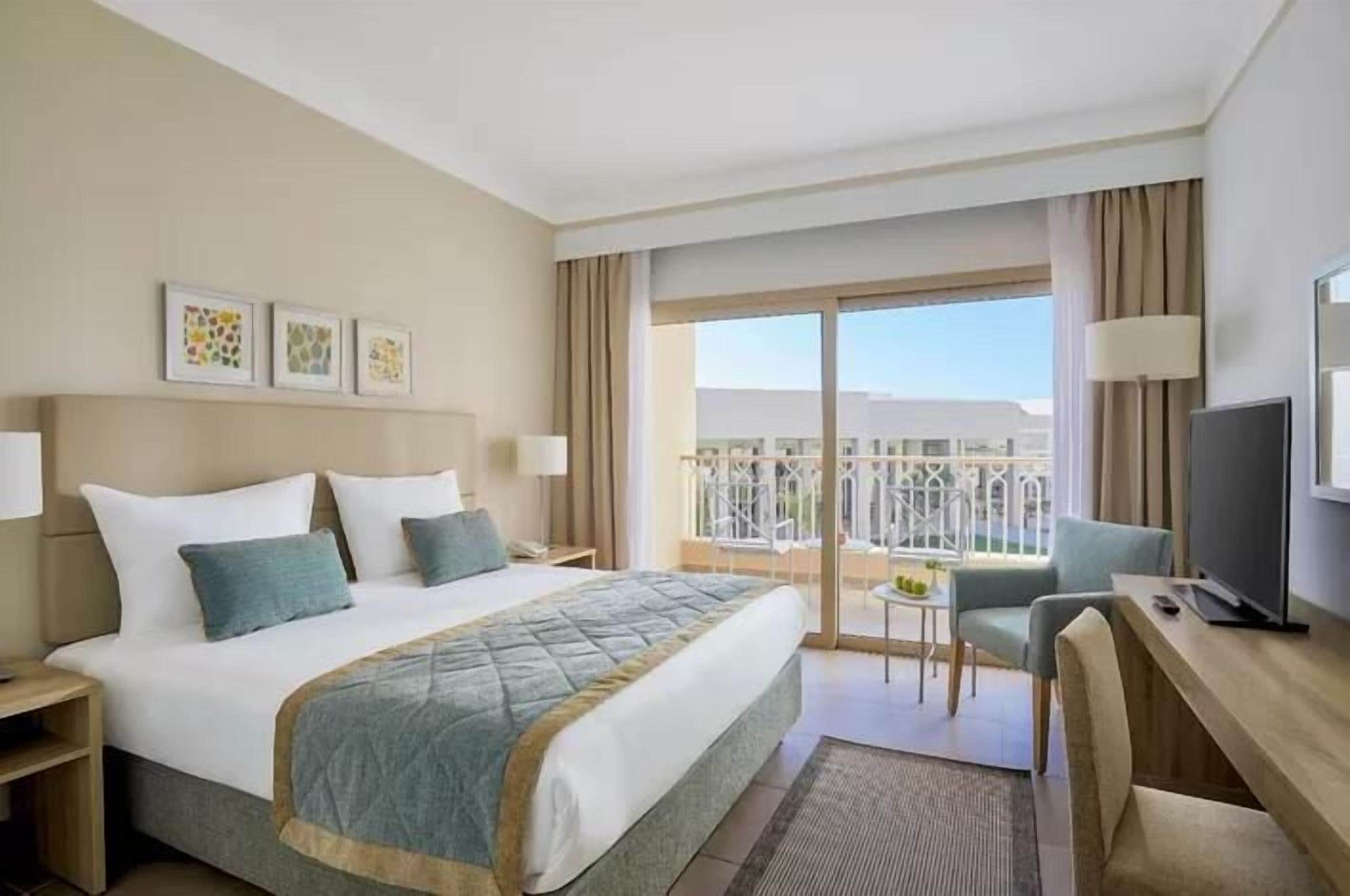 Une chambre d’hôtel équipée d’un lit, d’un bureau, d’une chaise, d’une télévision et d’un balcon avec vue.