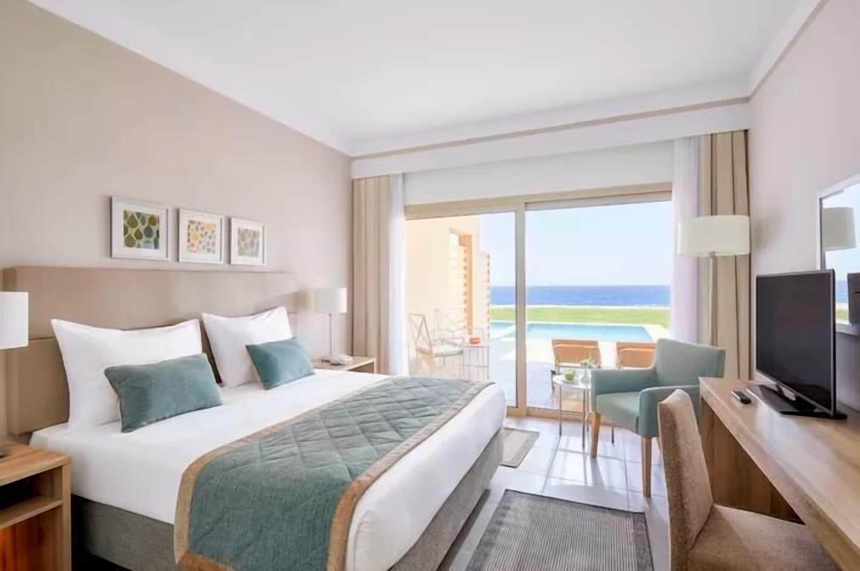 Ein Hotelzimmer mit Bett, Schreibtisch, Fernseher und einem Balkon mit Blick.