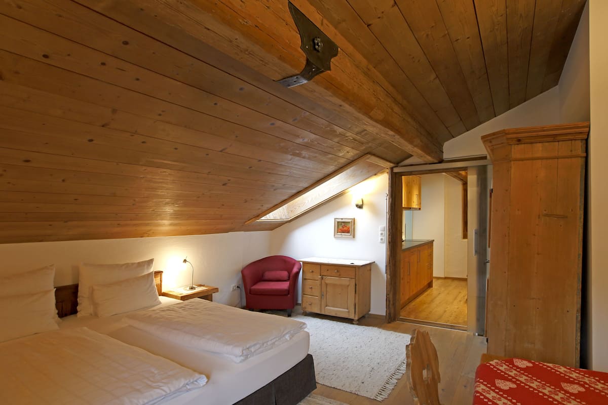A bedroom with a wooden ceiling, a bed, a red chair, a wooden cabinet, and a mirror.