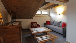Ett mysigt rum i loftstil med ett träpanelat tak, en soffa med röda och grå kuddar, ett träbord och en röd fåtölj.