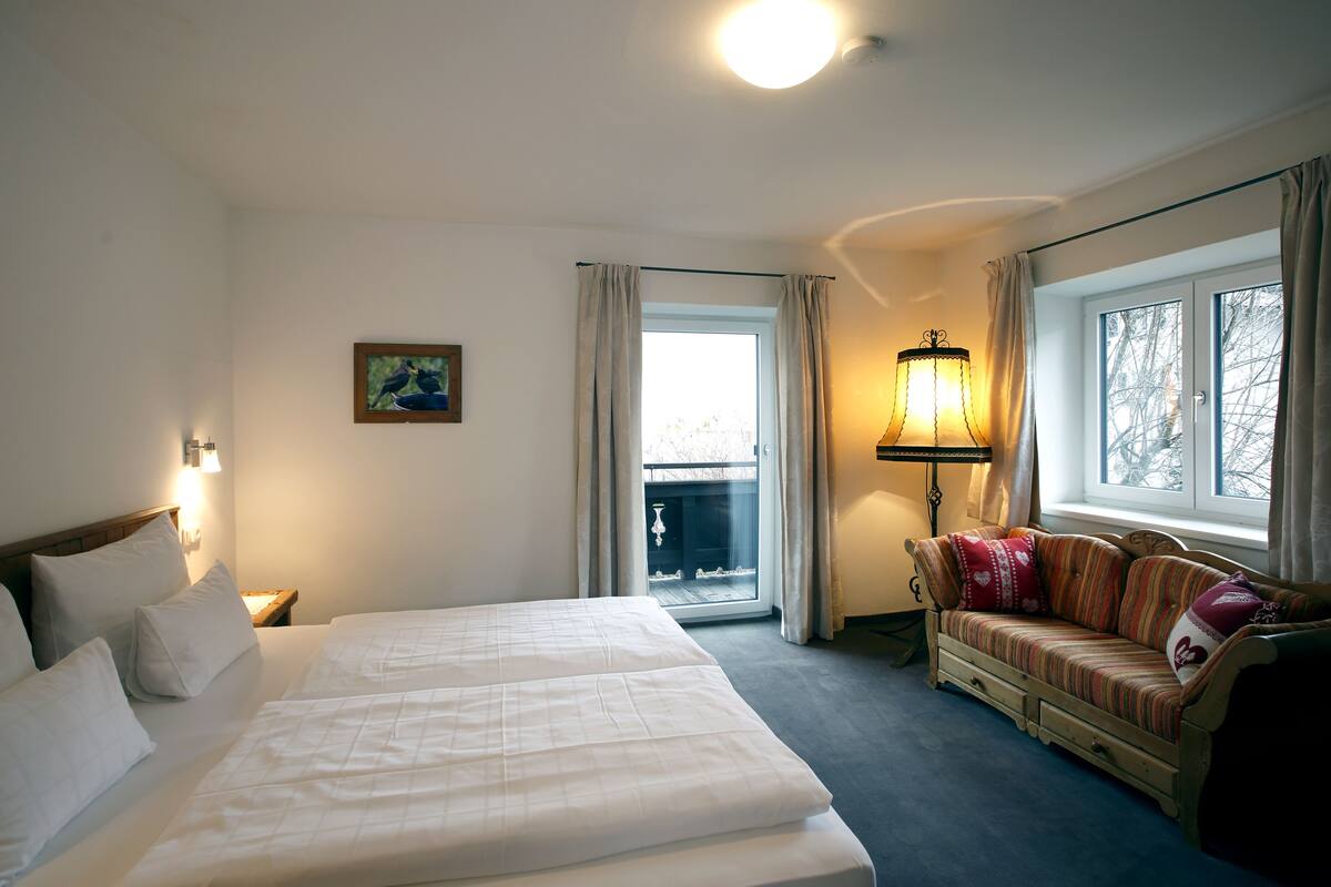 A hotel room with a bed, a sofa, a lamp, and a window with curtains.
