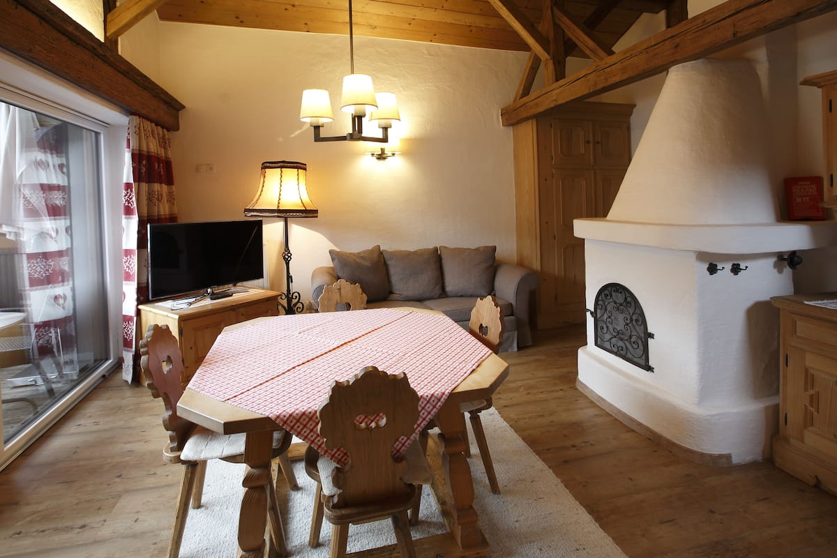 A cozy living room with a wooden table set for dining, a sofa, a television, and a fireplace.