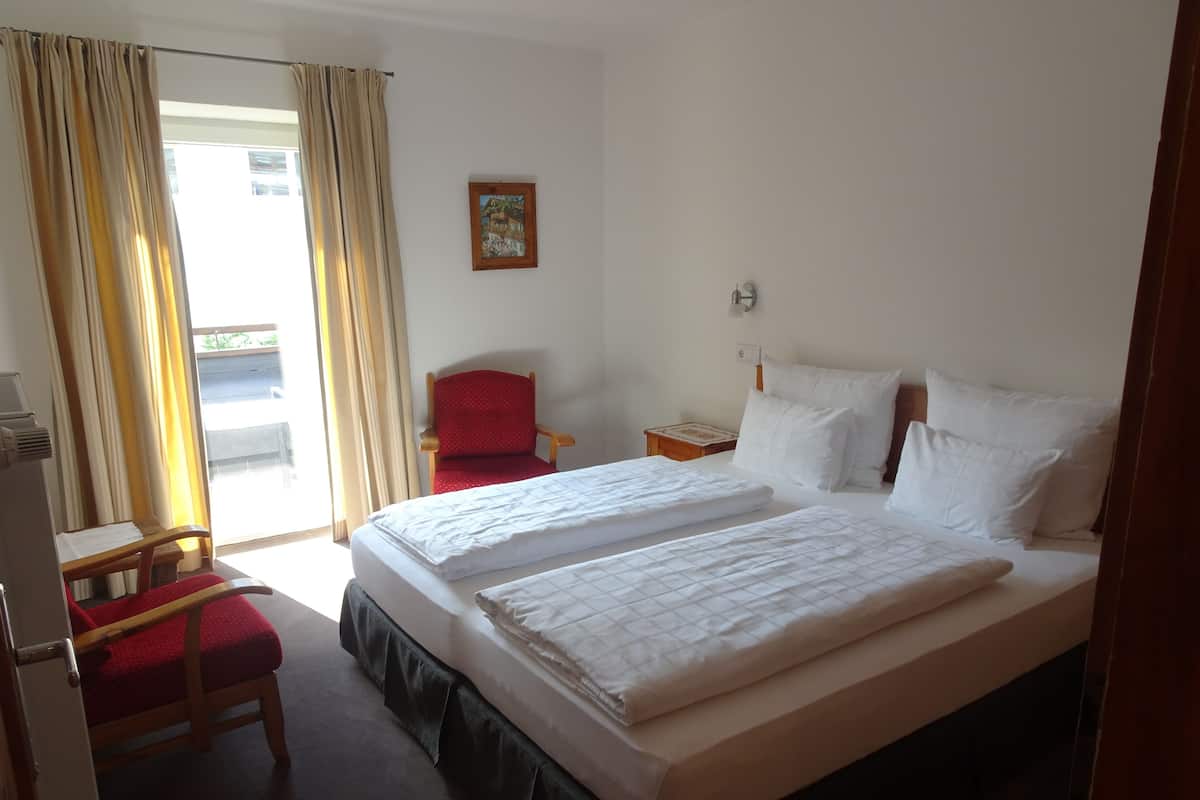 A hotel room with two beds, a red chair, a small table, and a window with curtains.