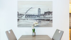 A dining area with a table, chairs, and a painting of a bridge and cityscape. - Thomas Street Apartments (Dublin)