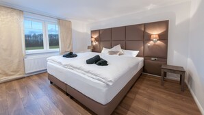 Une chambre d’hôtel moderne avec un grand lit, un plancher en bois, une fenêtre avec des rideaux et des luminaires fixés au mur.