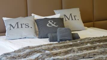 Una cama con tres almohadas etiquetadas como “Mrs.”, “&” y “Mr.”, y un par de toallas grises.