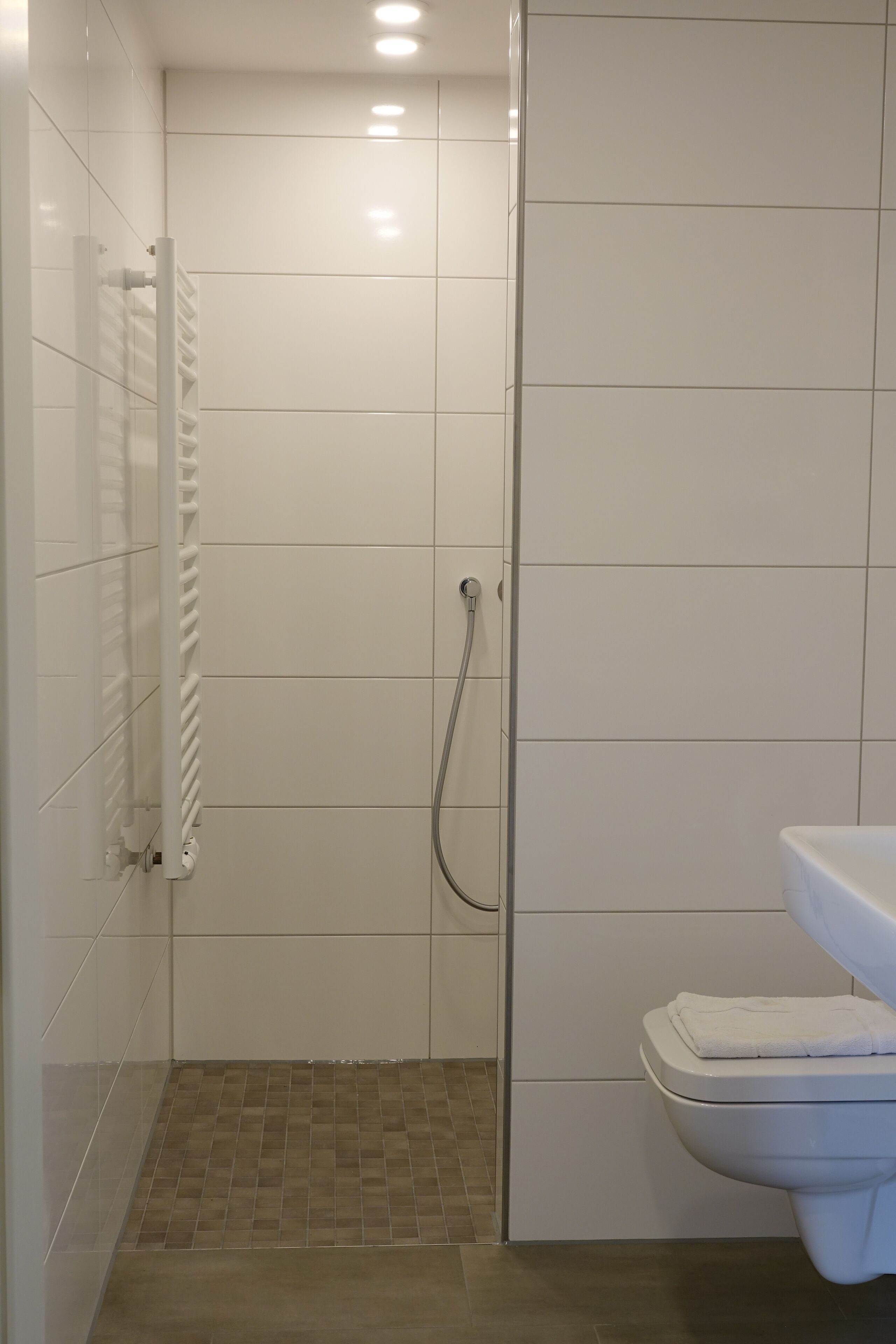 A bathroom with white tiles, a shower, a toilet, and a towel on the toilet.