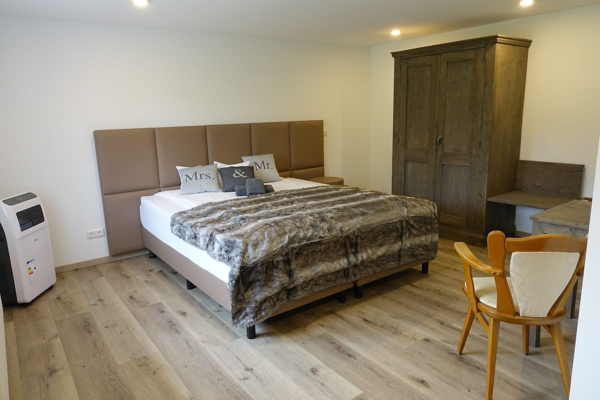 Un dormitorio con una cama, un armario de madera, una silla y un calentador.