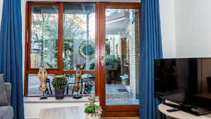 Una sala de estar con puerta corrediza de vidrio que da a un balcón, un televisor sobre un mueble bajo y una planta en maceta en el alféizar.