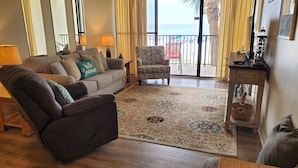 A living room with a sofa, armchair, and a view of the beach through large windows. - Beach Front Condo PCB! Spring/Fall and Winter Discount Rates Available Now!! (Panama City Beach)