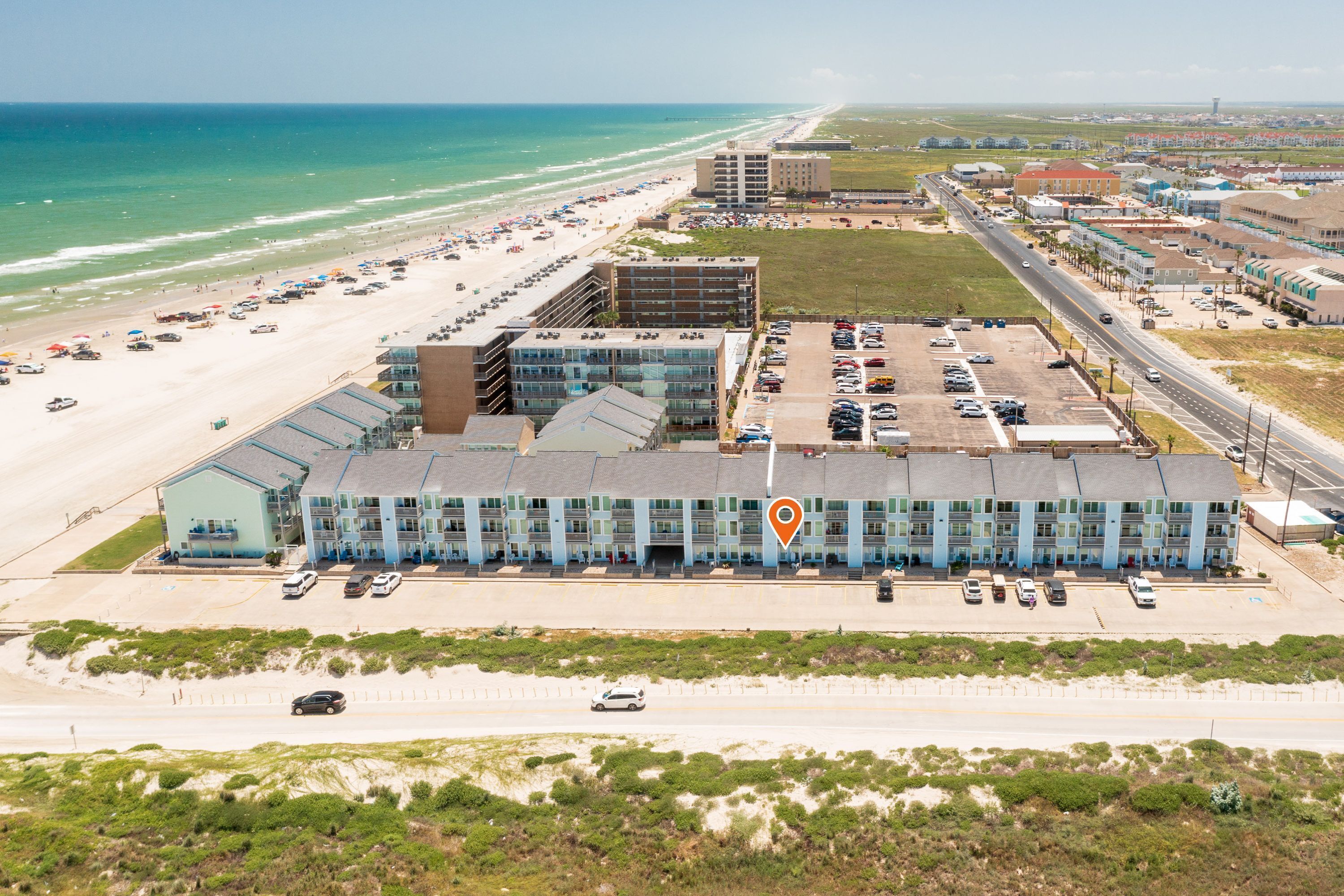 An aerial view of a coastal hotel with a parking lot, beach access, and a view of the ocean.