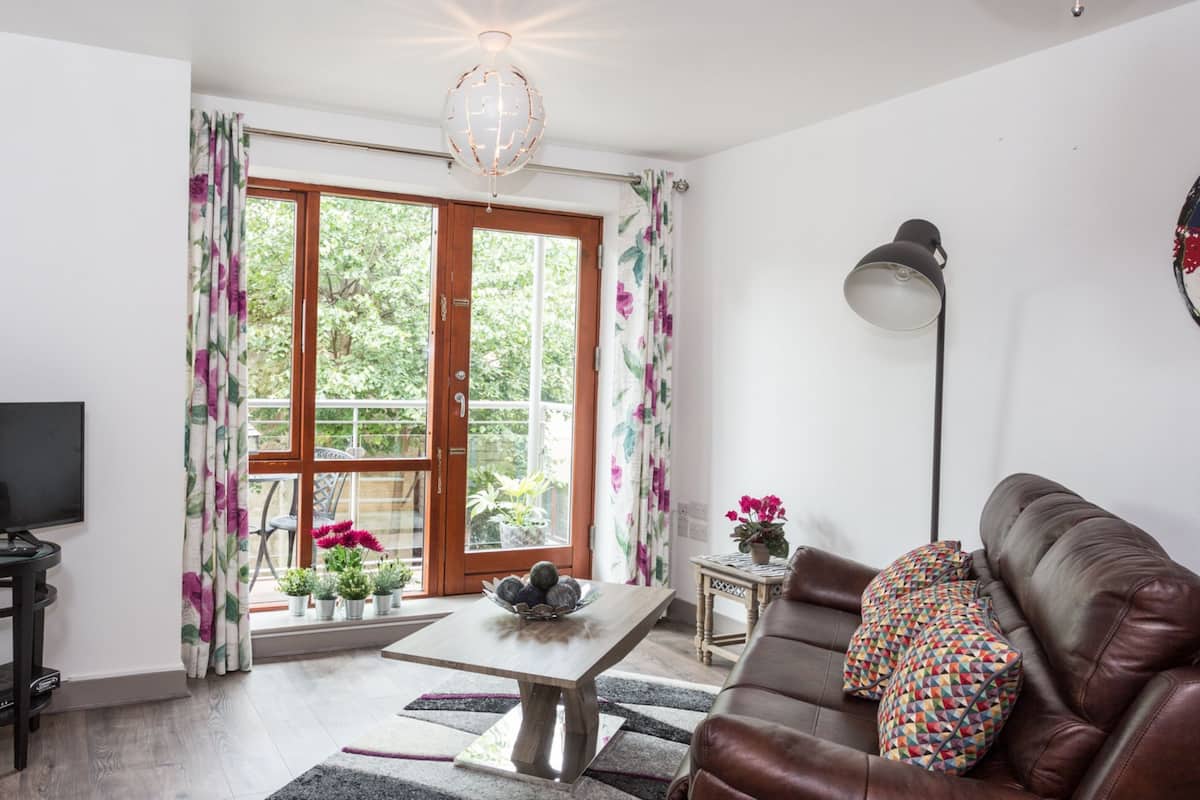 A living room with a television, sofa, table, and potted plants near a window.
