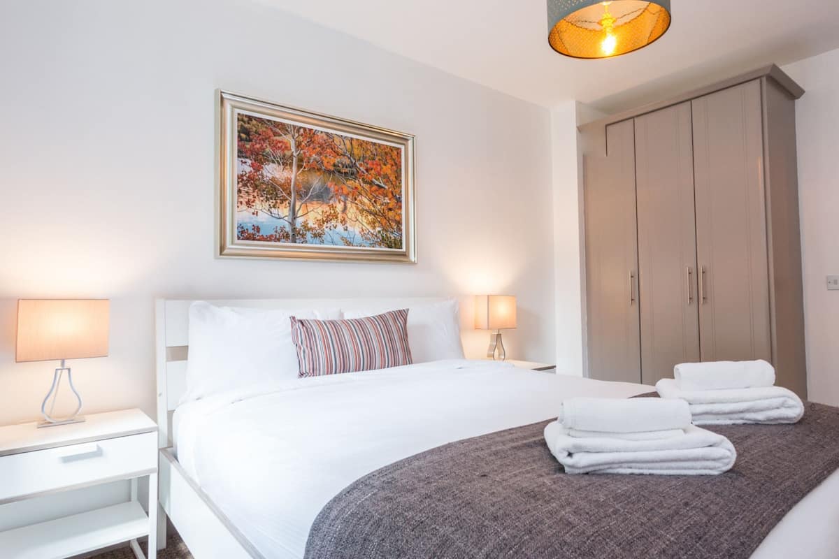 A hotel room with a bed, two bedside lamps, a framed picture on the wall, a wardrobe, and a door.