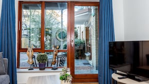 Una sala de estar con puerta corrediza de vidrio que da a un balcón, un televisor sobre un mueble bajo y una planta en maceta en el alféizar.