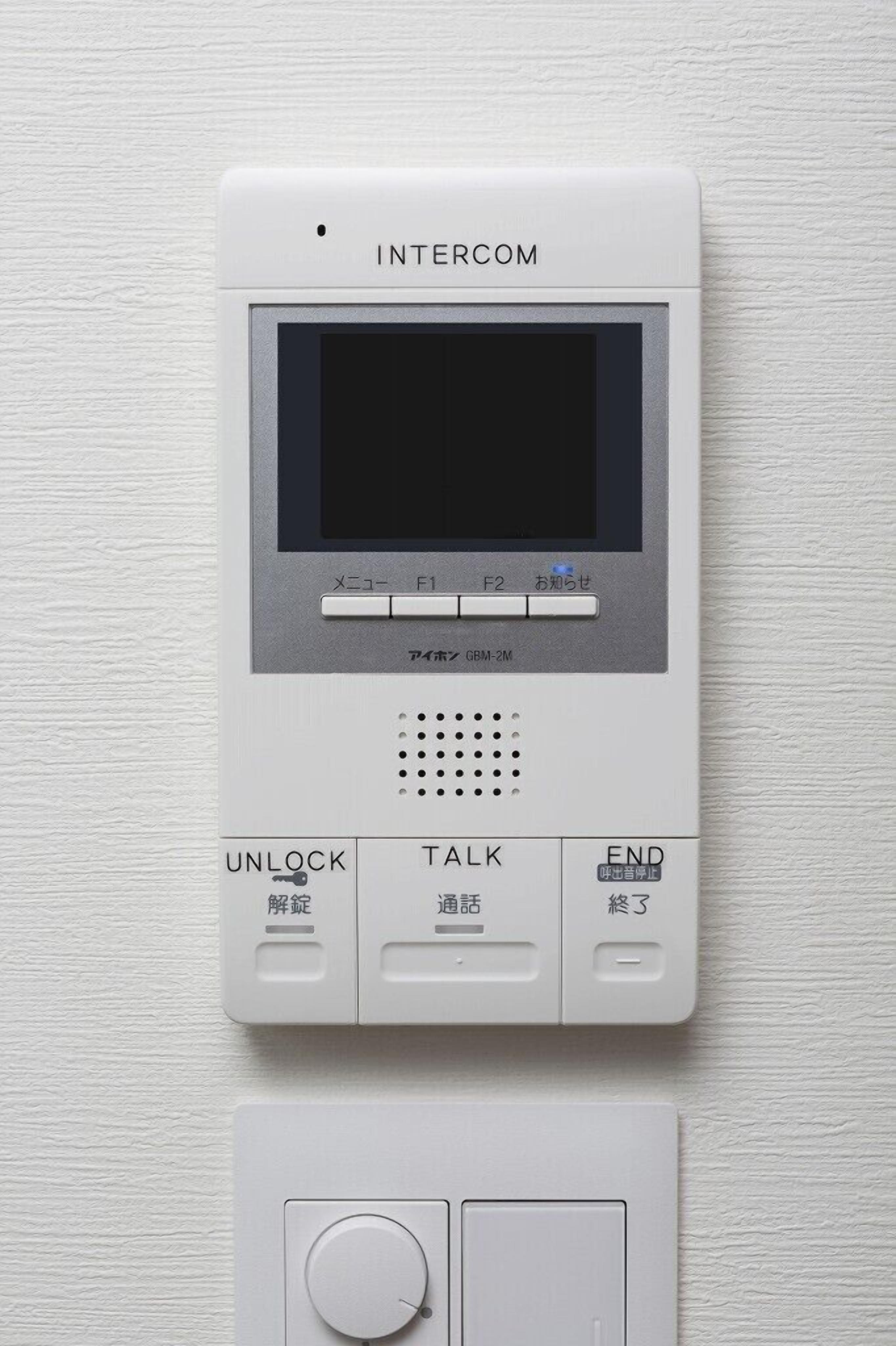 Un dispositivo de intercomunicador blanco con pantalla, botones etiquetados 'Desbloquear', 'Hablar' y 'Finalizar', y un teclado en la parte inferior.