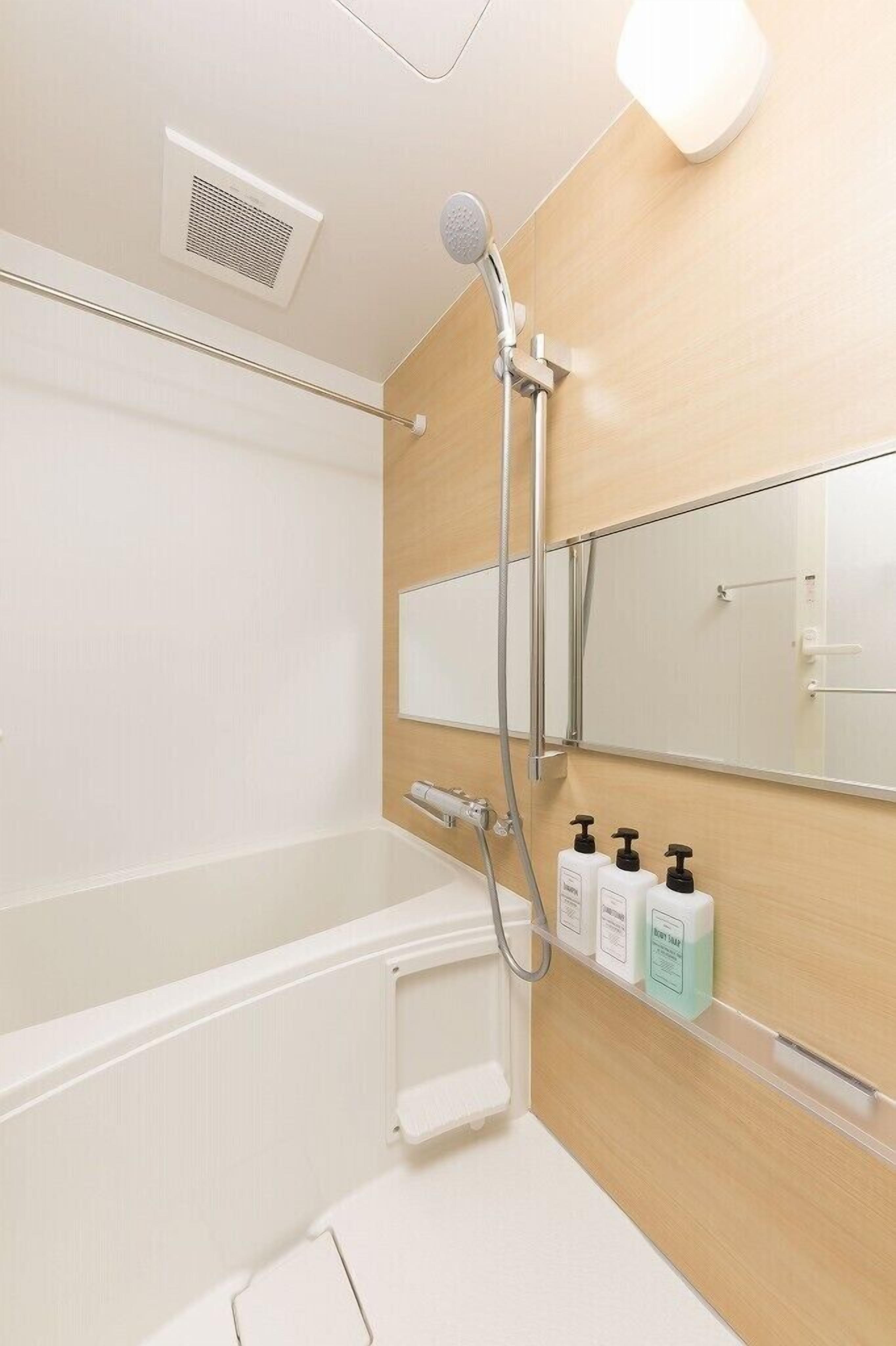 A modern bathroom with a bathtub, a showerhead, a mirror, and toiletries on a shelf.