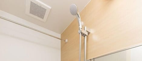 A modern bathroom with a bathtub, a showerhead, a mirror, and toiletries on a shelf.
