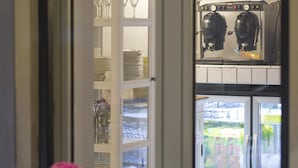 Udsigt gennem et vindue ind til et rum med et tekøkken, inklusive et køleskab fyldt med drikkevarer og en kaffemaskine.