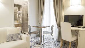 Et hotelværelse med en glas brusekabine, et spisebord med stole, et fjernsyn og en sofa.