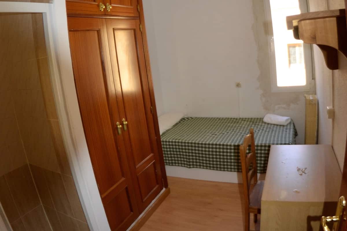 Una habitación pequeña con un armario de madera, una mesita, una silla y una ventana con vistas.